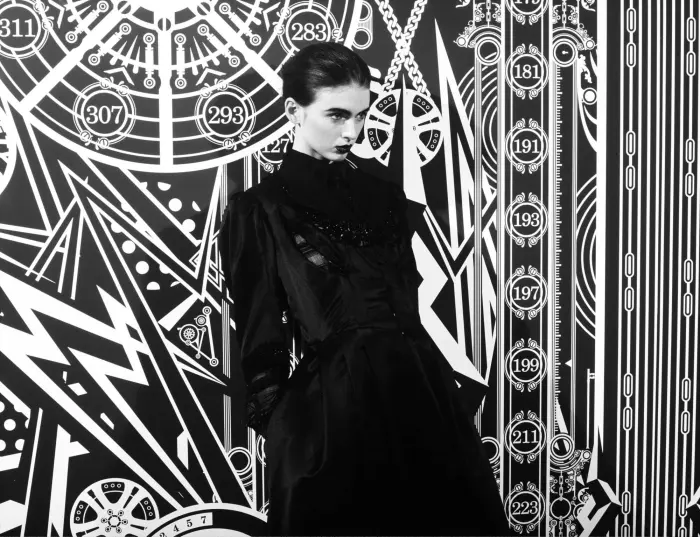 Woman in a black dress standing in front of patterned wallpaper